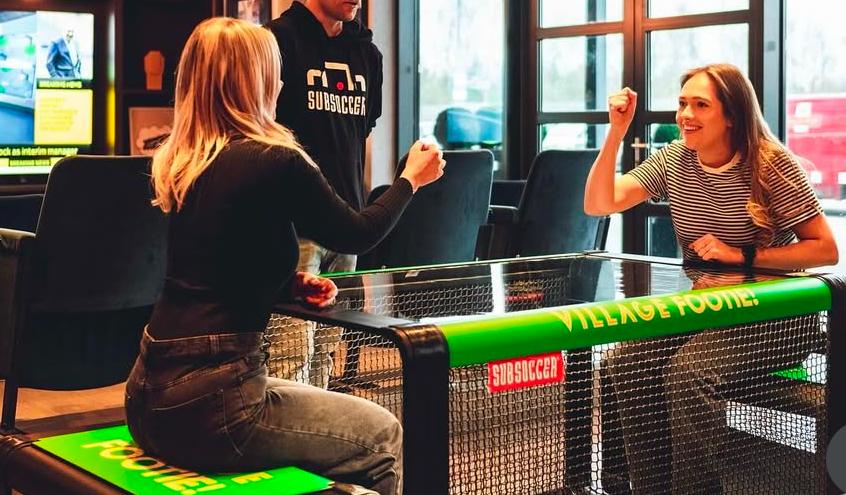 Two women celebrating a goal playing SubSoccer bench soccer in an office or co-working space