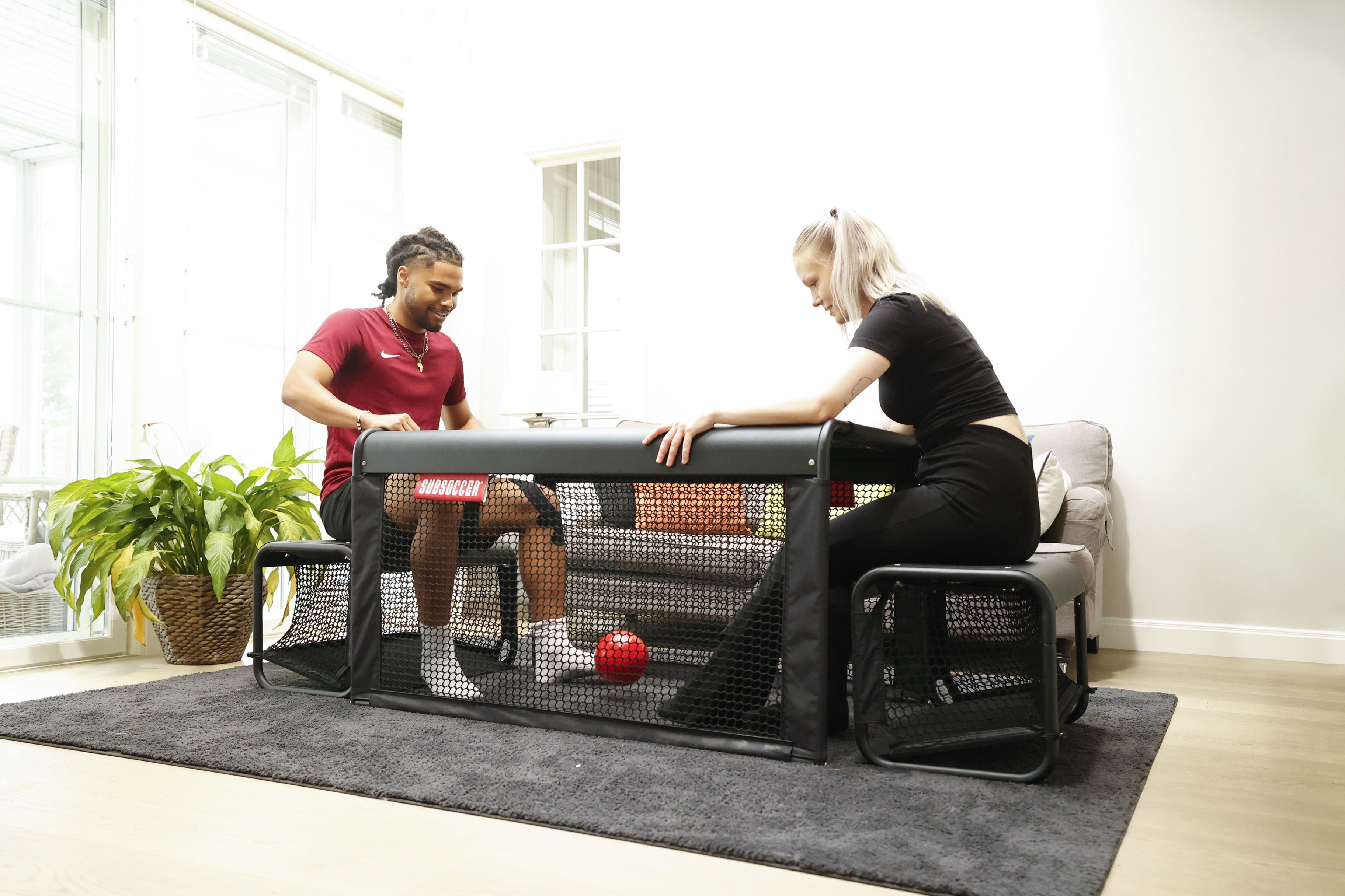 Man and woman playing SubSoccer S7 bench soccer game face to face on an indoor rug